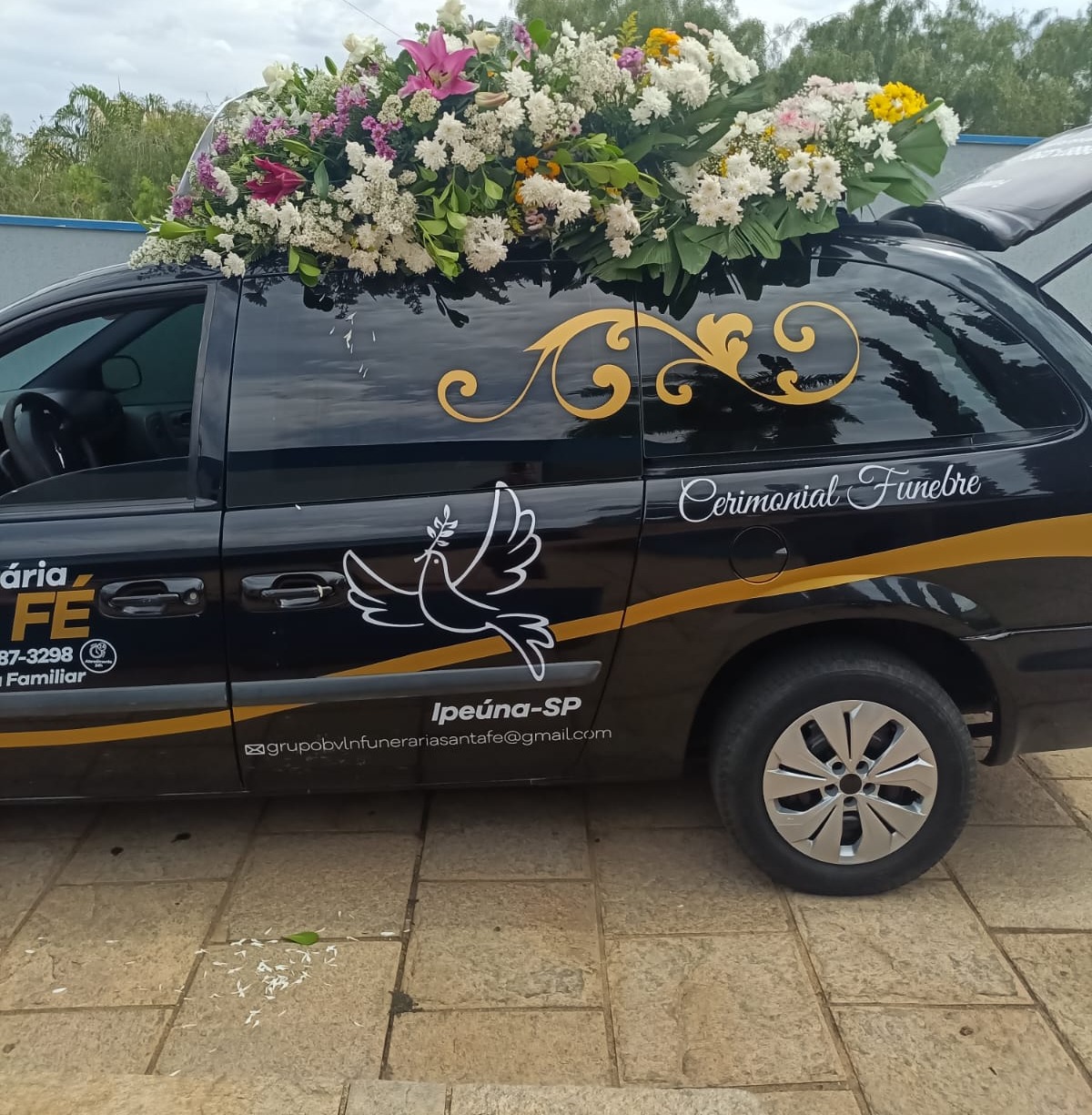 Carro funerário da Funerária Santa Fé com arranjo floral no teto, pronto para o cerimonial fúnebre